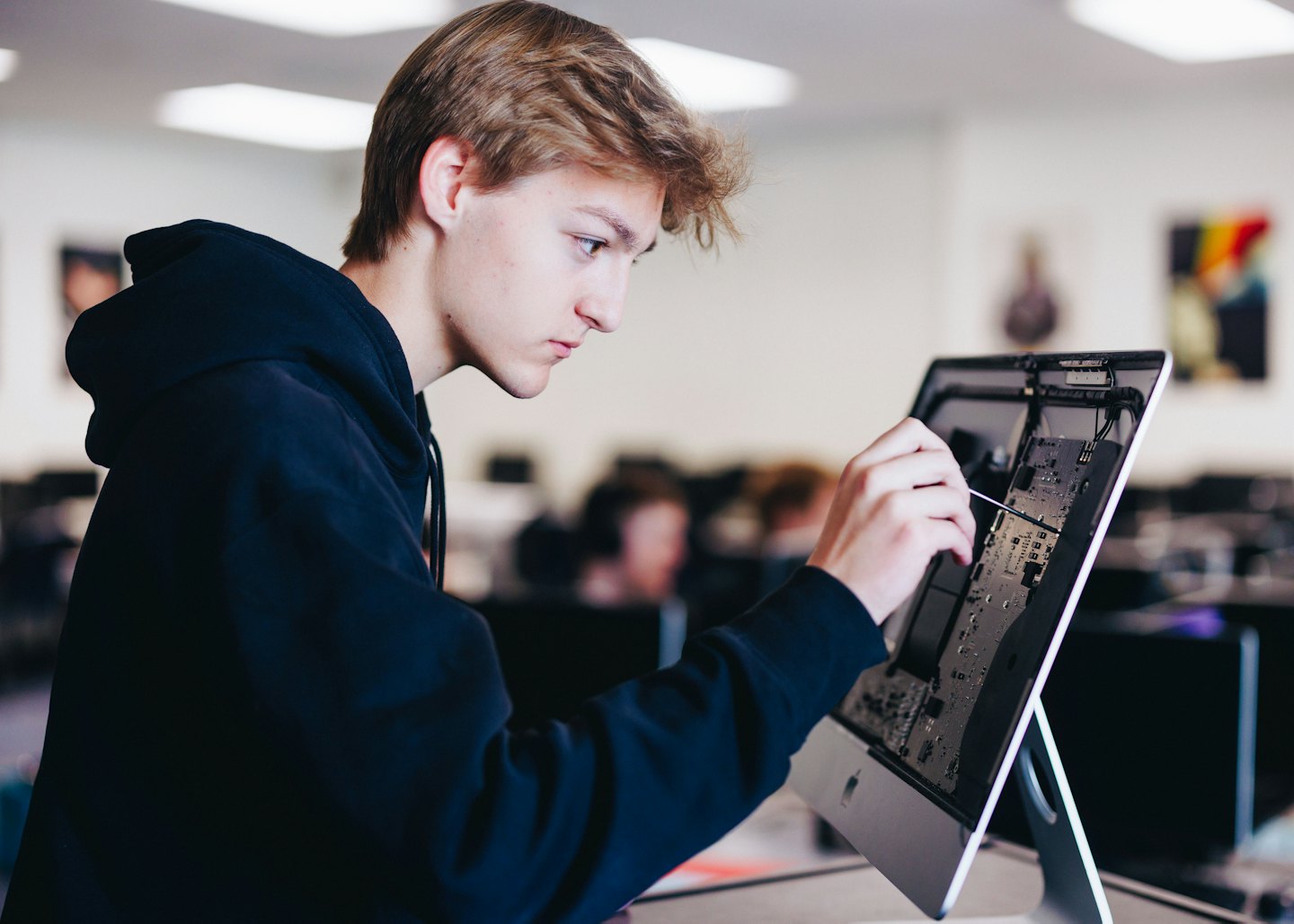 Man repairs computer circuit board in classroom lab.
