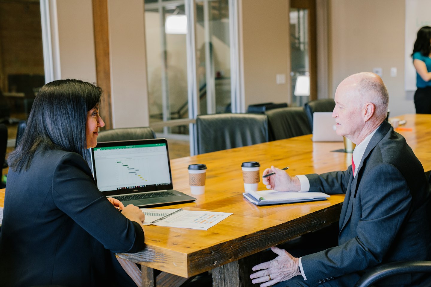 Business professionals discuss a chart on a laptop at a conference table.