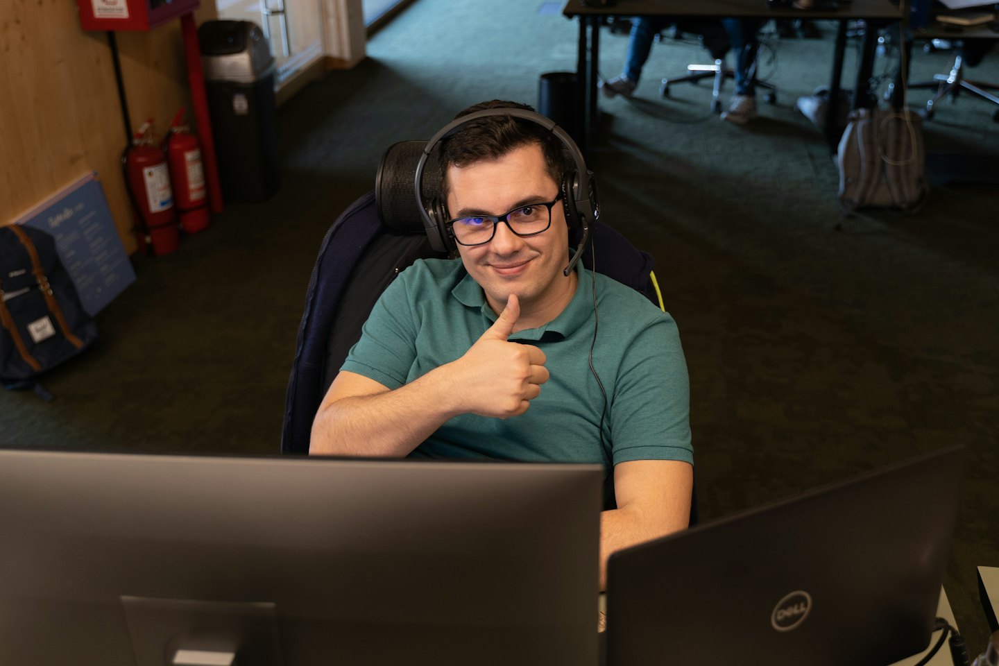 Man in headset gives thumbs-up at office desk.